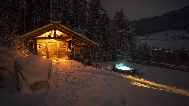 Eine Holzhütte mit beleuchtetem Inneren, umgeben von schneebedeckten Bäumen und einer verschneiten Landschaft.