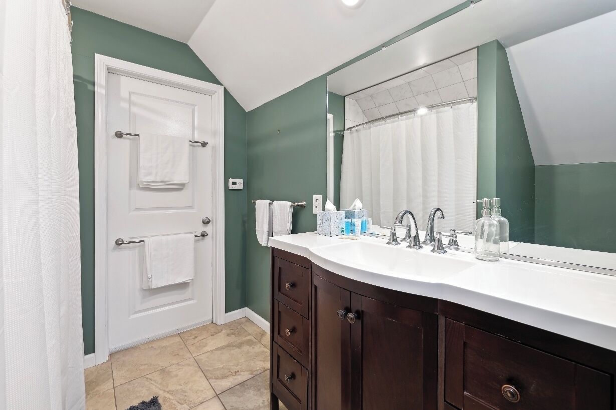 Une salle de bain avec un meuble-lavabo blanc, un grand miroir et un mur vert.