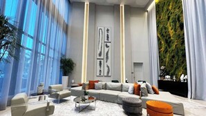 A modern living room with a sectional sofa, ottomans, a coffee table, and a large window with sheer curtains. - Luxury Condo - 3B/3B with Amazing Skyline View (Doral)