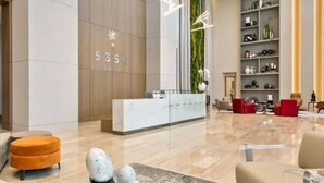 A modern hotel lobby with a reception desk, a large wall with a vertical garden, and a seating area with red and beige chairs. - Luxury Condo - 3B/3B with Amazing Skyline View (Doral)