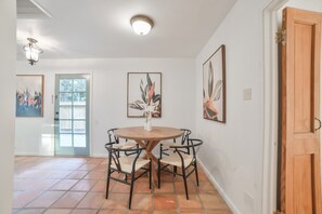A dining area with a round table, four chairs, and a vase of flowers. There are two doors, one with a frosted glass panel and another with a wooden frame. - Charming Fig Garden Village Spanish style home! (Fresno)