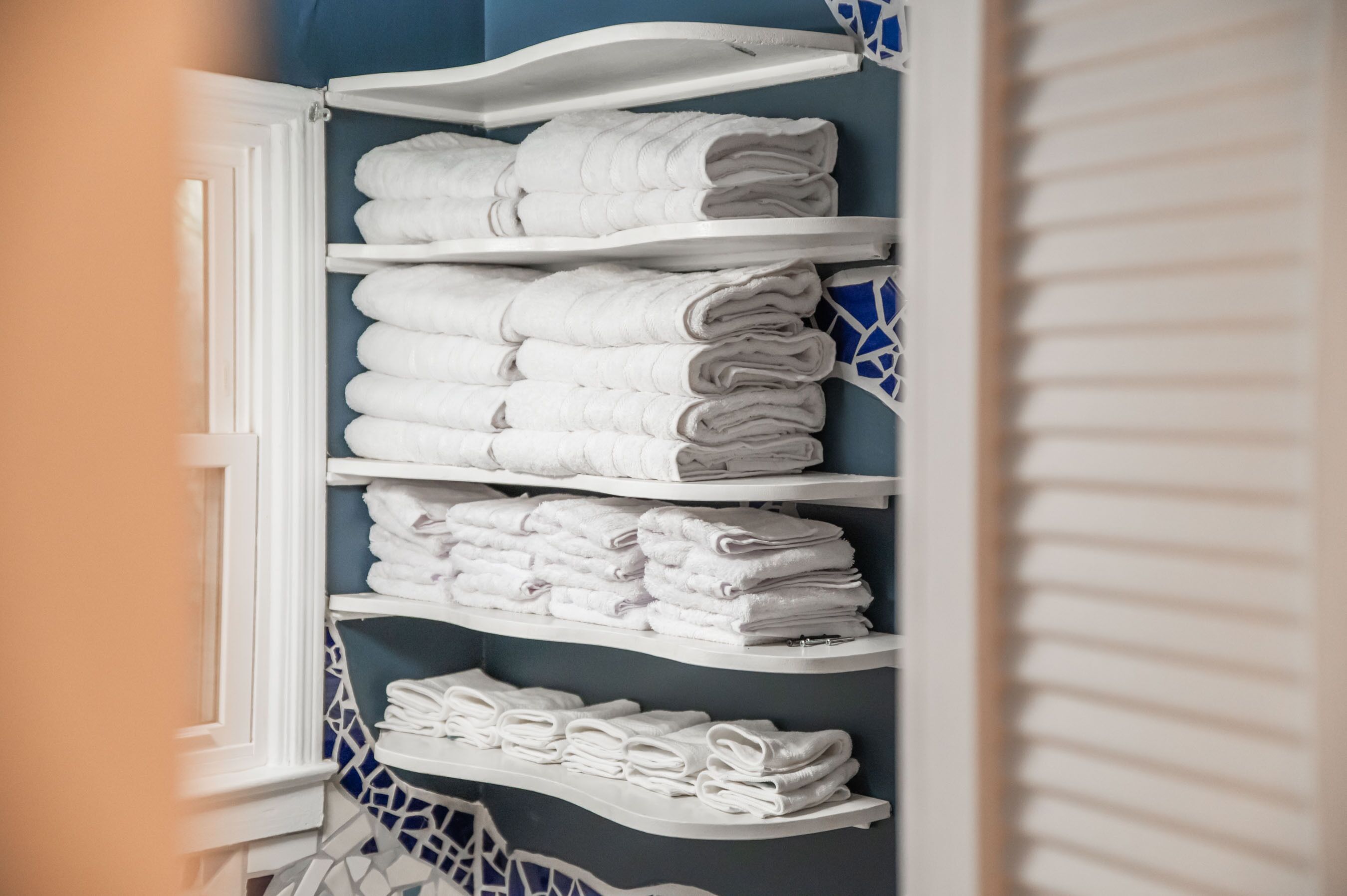 A bathroom with white shelves holding neatly folded towels.