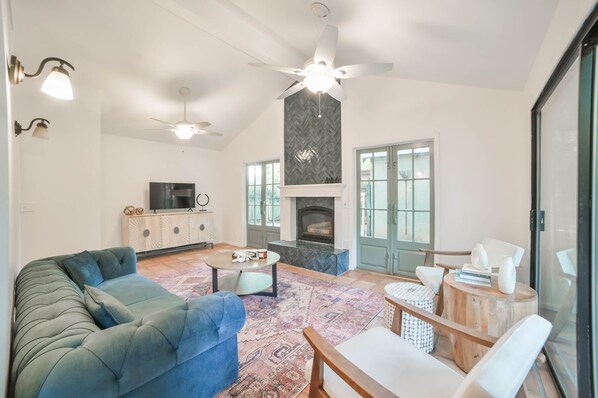 A spacious living room with a fireplace, a ceiling fan, and a large window. - Charming Fig Garden Village Spanish style home! (Fresno)