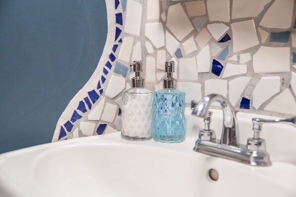Ein Waschbecken mit zwei Seifenspendern, einem Wasserhahn und einer Rückwand aus Mosaikfliesen.