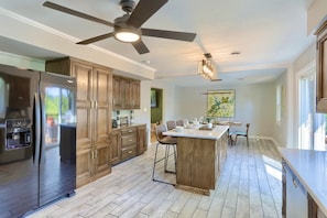 A modern kitchen with wooden cabinets, a stainless steel refrigerator, a ceiling fan, and a dining area with a bar stool.
