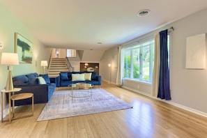 A spacious living room with a blue sofa, a coffee table, and a large window with curtains.