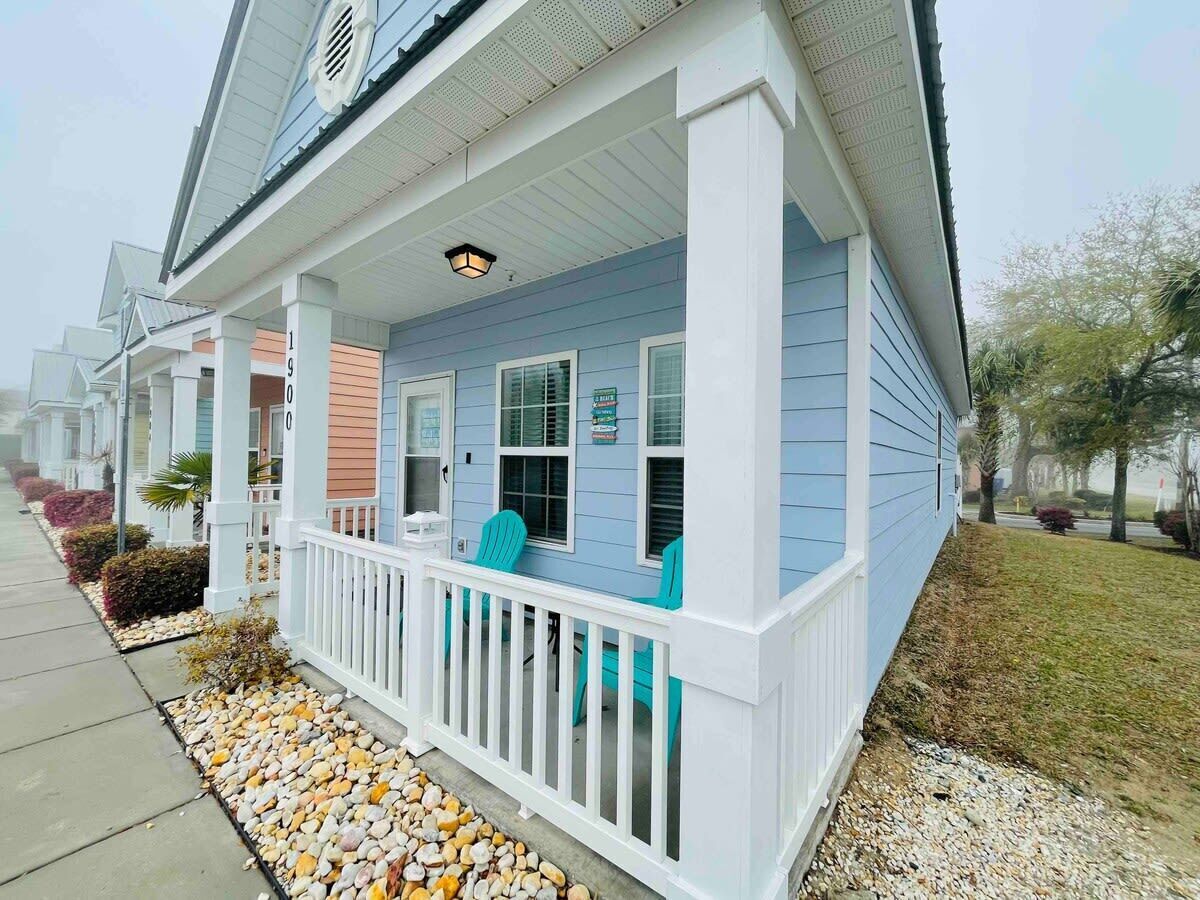 A single-story house with a covered porch, a small front yard with pebbles, and a street view with other houses.