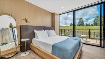 A modern bedroom with a large bed, a bedside table, a mirror, and a view of the outdoors.