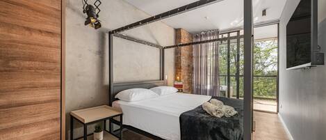 Un dormitorio moderno con una cama con dosel, una mesita de noche pequeña y un buró, y un gran ventanal con vistas al exterior.