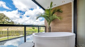 Un baño moderno con una bañera grande, una mesita redonda pequeña y vistas a una piscina y vegetación.
