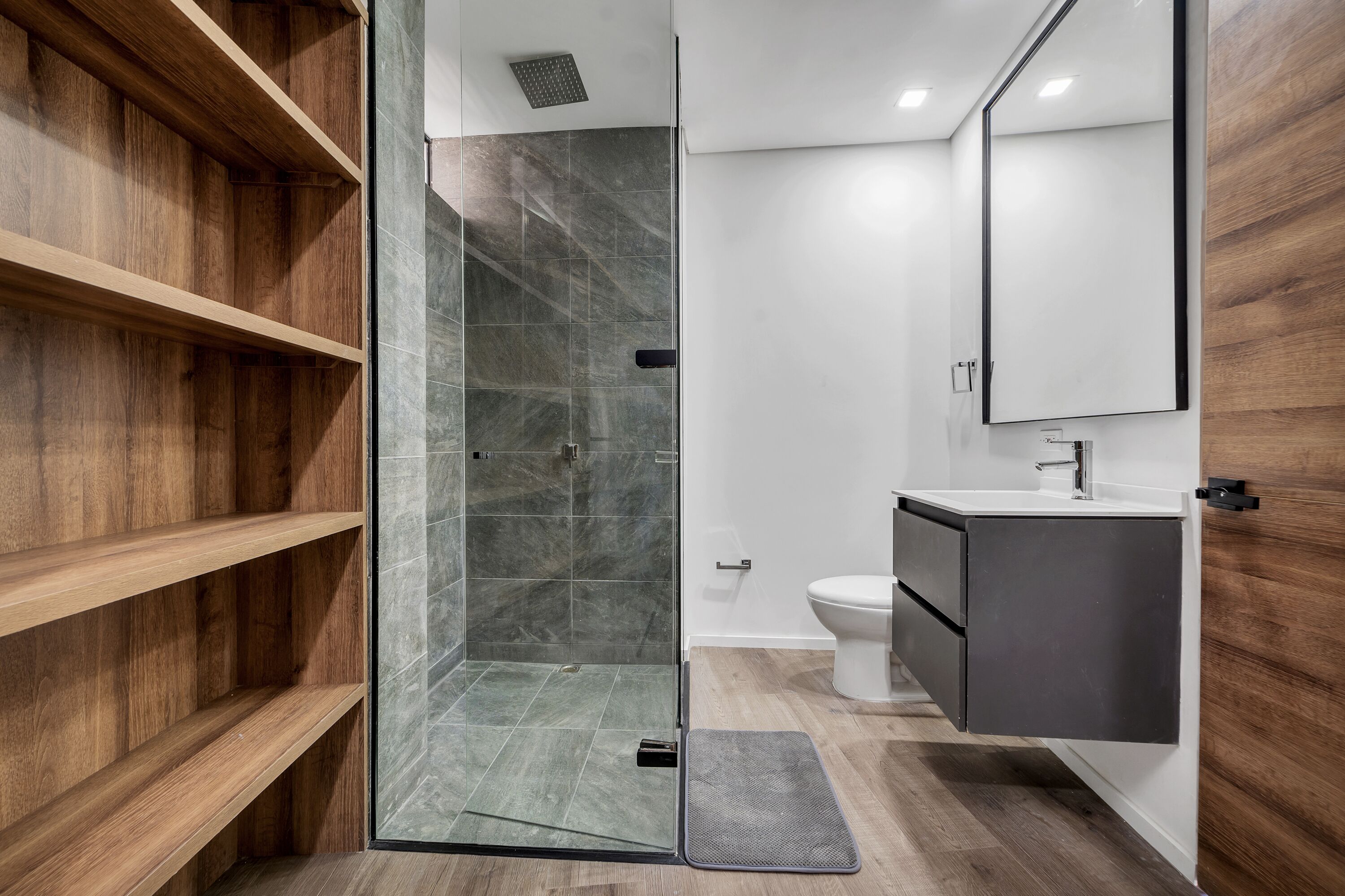 Un bagno moderno con doccia a vetro, mensole in legno, un lavandino bianco e uno specchio grande.