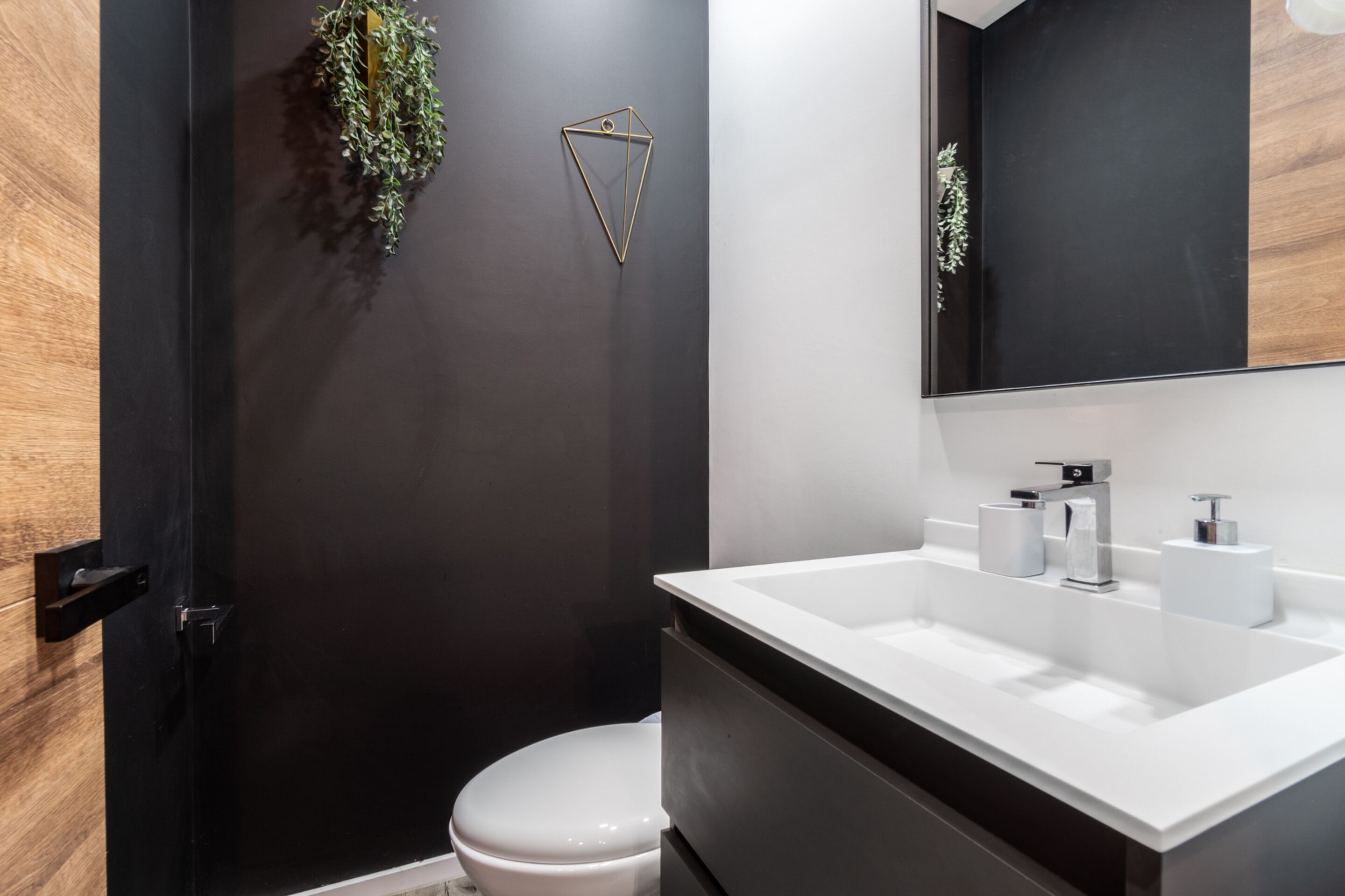 A modern bathroom with a black wall, a white sink, and a mirror above it.