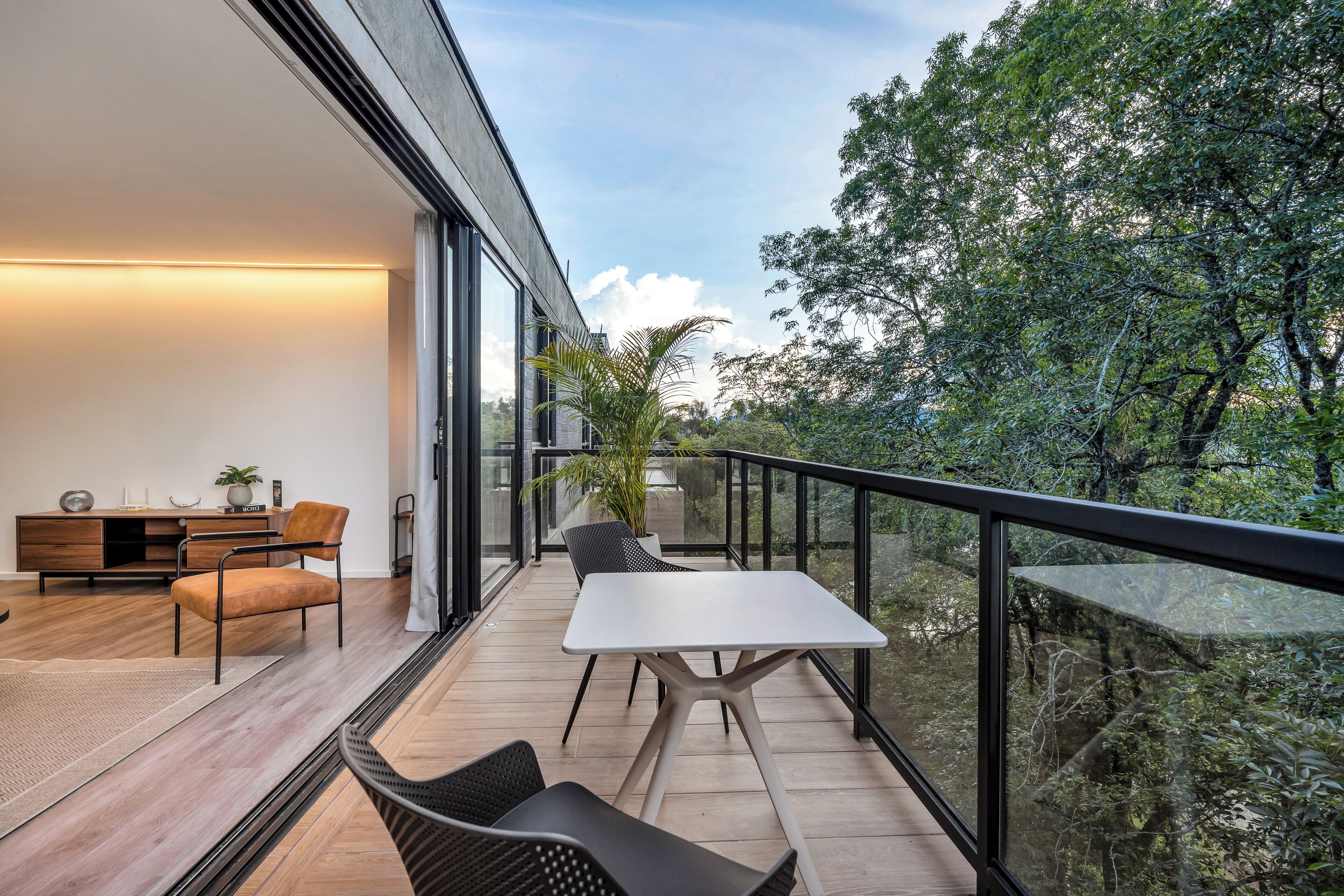 A modern balcony with a dining area, including a table and chairs, overlooking a lush garden.