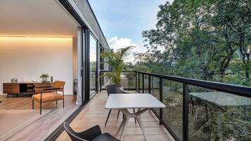 A modern balcony with a dining area, including a table and chairs, overlooking a lush garden.