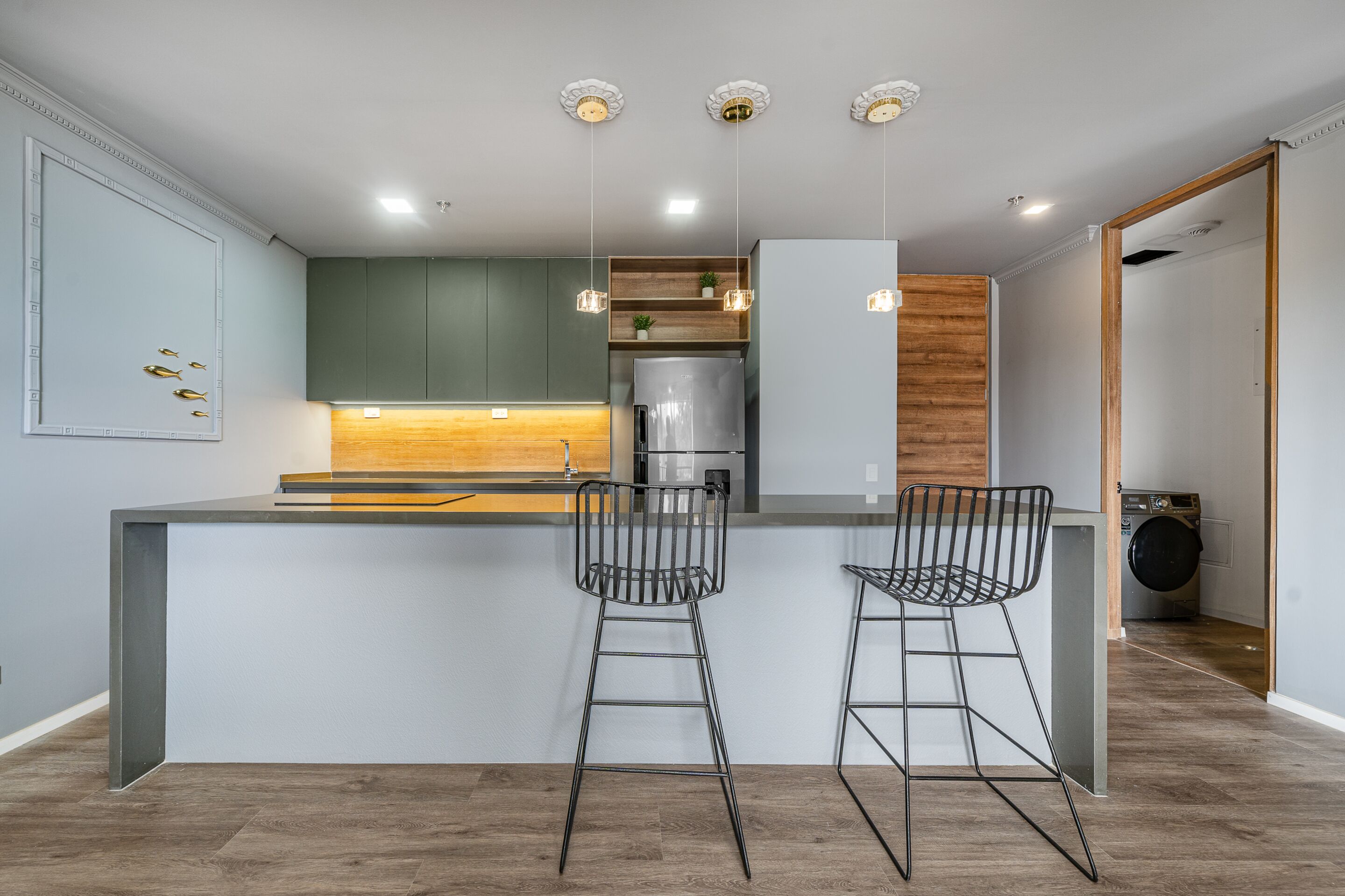 Una cocina moderna con una isla central, taburetes de bar y lavadora integrada.