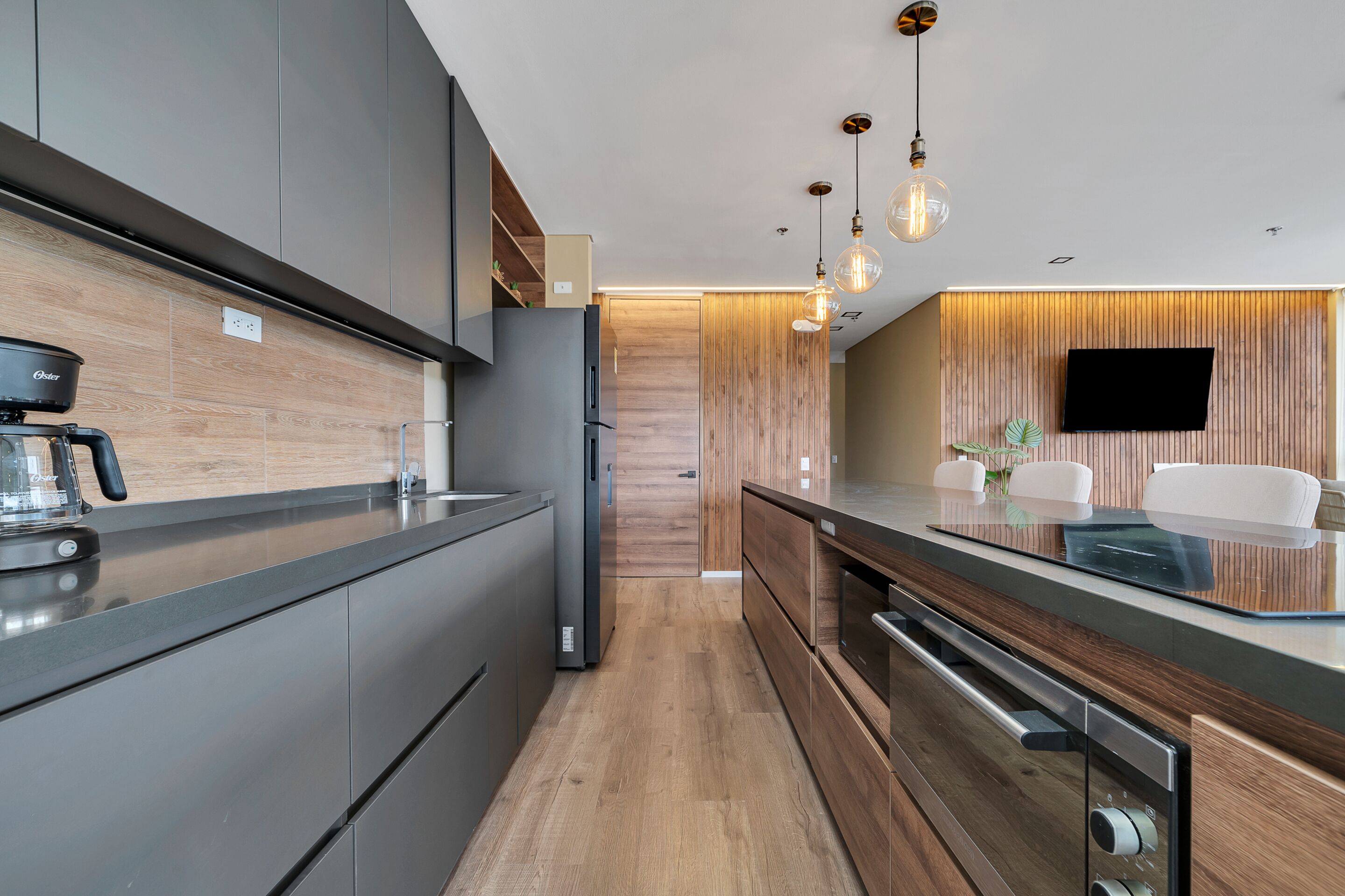 A modern kitchen with a built-in oven, a coffee maker, and a flat-screen TV mounted on the wall.