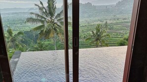 Une personne se détend dans une baignoire en verre, d’où elle peut admirer un paysage luxuriant et des palmiers.