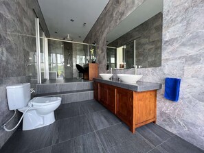 Une salle de bain moderne avec un mur en marbre, un meuble-lavabo en bois, deux vasques et des toilettes.