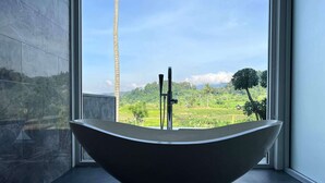 Une salle de bain moderne avec une baignoire sur pieds, de grandes fenêtres et une vue sur un paysage verdoyant.