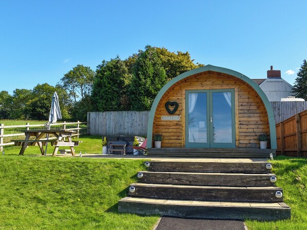 Une petite cabane en bois, ornée d’un décor en forme de cœur au-dessus de la porte, avec une enseigne indiquant « Le repaire de Jacob », et une table de pique-nique à l’arrière-plan.