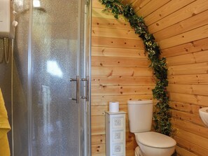 Une salle de bain rustique, aménagée dans une cabane en bois, avec une douche en verre, des toilettes et un meuble orné de sculptures décoratives.