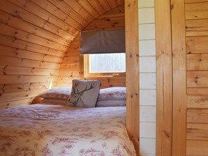 Une chambre confortable dans un chalet, avec des murs en bois, un lit recouvert d’une literie à motifs floraux et une fenêtre offrant une belle vue.