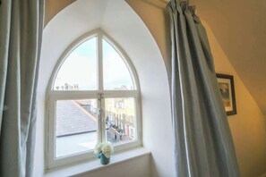 A room with a large arched window, a small table with a vase, and a framed picture on the wall.