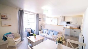 A living room with a sofa, a dining table, and a kitchen area with cabinets and a microwave. - Elizabeth | Seaside charm | Iconic location (Ramsgate)