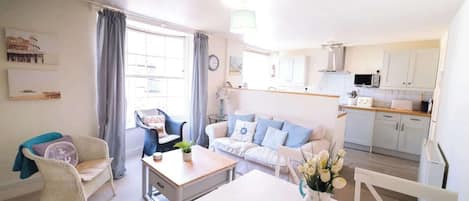 A living room with a sofa, a dining table, and a kitchen area with cabinets and a microwave.