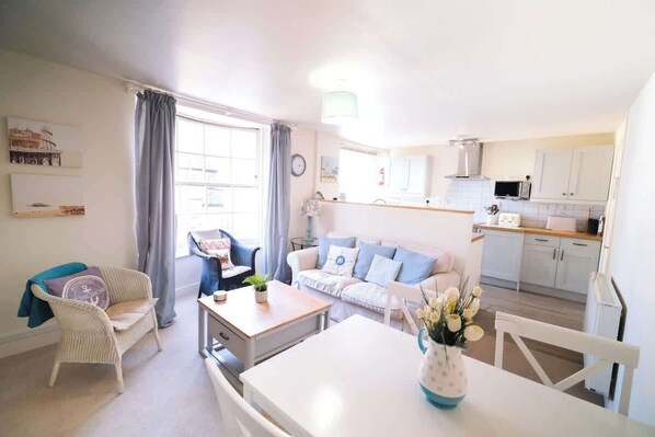 A living room with a sofa, a dining table, and a kitchen area with cabinets and a microwave.