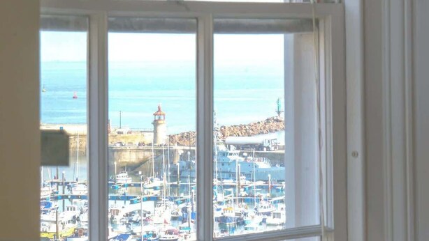 A view through a window of a marina with boats, a lighthouse, and rocky terrain. - Elizabeth | Seaside charm | Iconic location (Ramsgate)