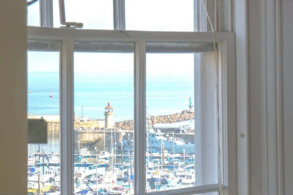 A view through a window of a marina with boats, a lighthouse, and rocky terrain.