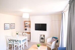 A living room with a dining table, chairs, a TV, a fireplace, and a bookshelf.