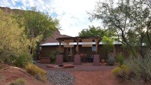 A rustic building with a covered patio area, surrounded by natural vegetation and a gravel path. - Desert Oasis & Spa - 30 Night Rental - Kayenta, Tuacahn & Zion  (Ivins)