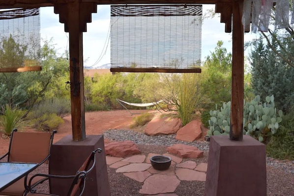 An outdoor patio with a table and chairs, a hammock, and a view of desert vegetation.