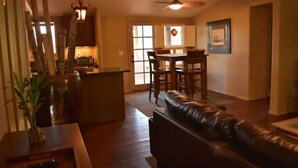 A spacious living room with a leather sofa, wooden flooring, and a dining area with a table and chairs. - Desert Oasis & Spa - 30 Night Rental - Kayenta, Tuacahn & Zion  (Ivins)