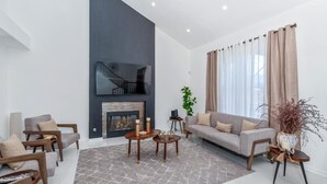 Una sala de estar moderna con chimenea, un sofá, dos sillones, una mesita de centro y un televisor montado en la pared.