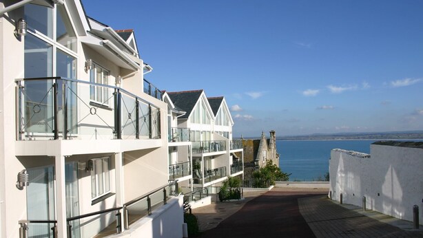 A coastal hotel with multiple balconies, a view of the sea, and a stone tower in the background. - Indigo (St Ives)