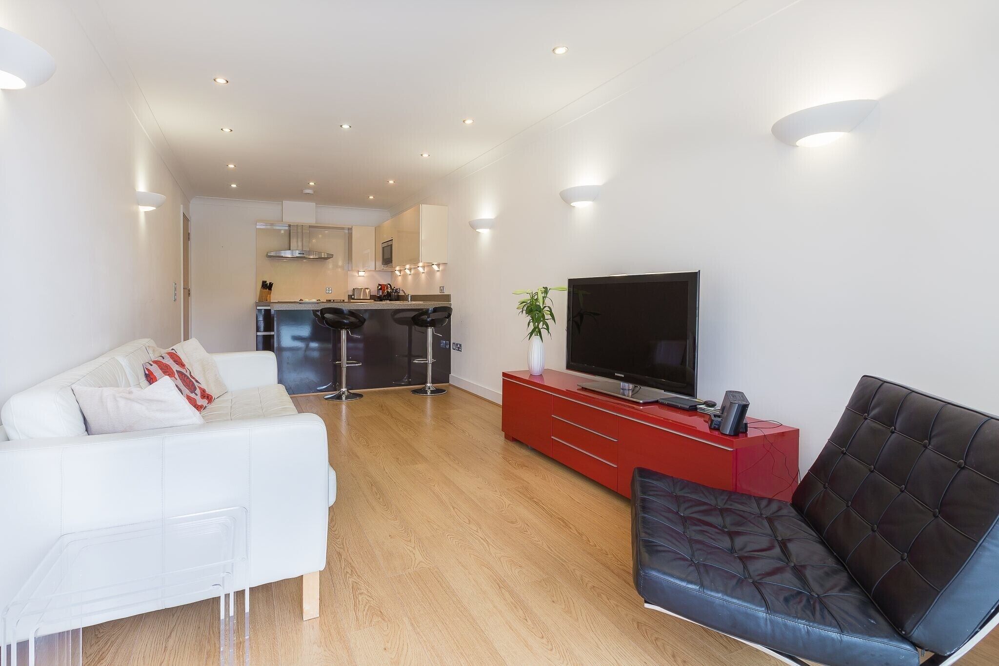 Un salon moderne avec un canapé blanc, un fauteuil en cuir noir, un meuble de rangement rouge et un téléviseur.