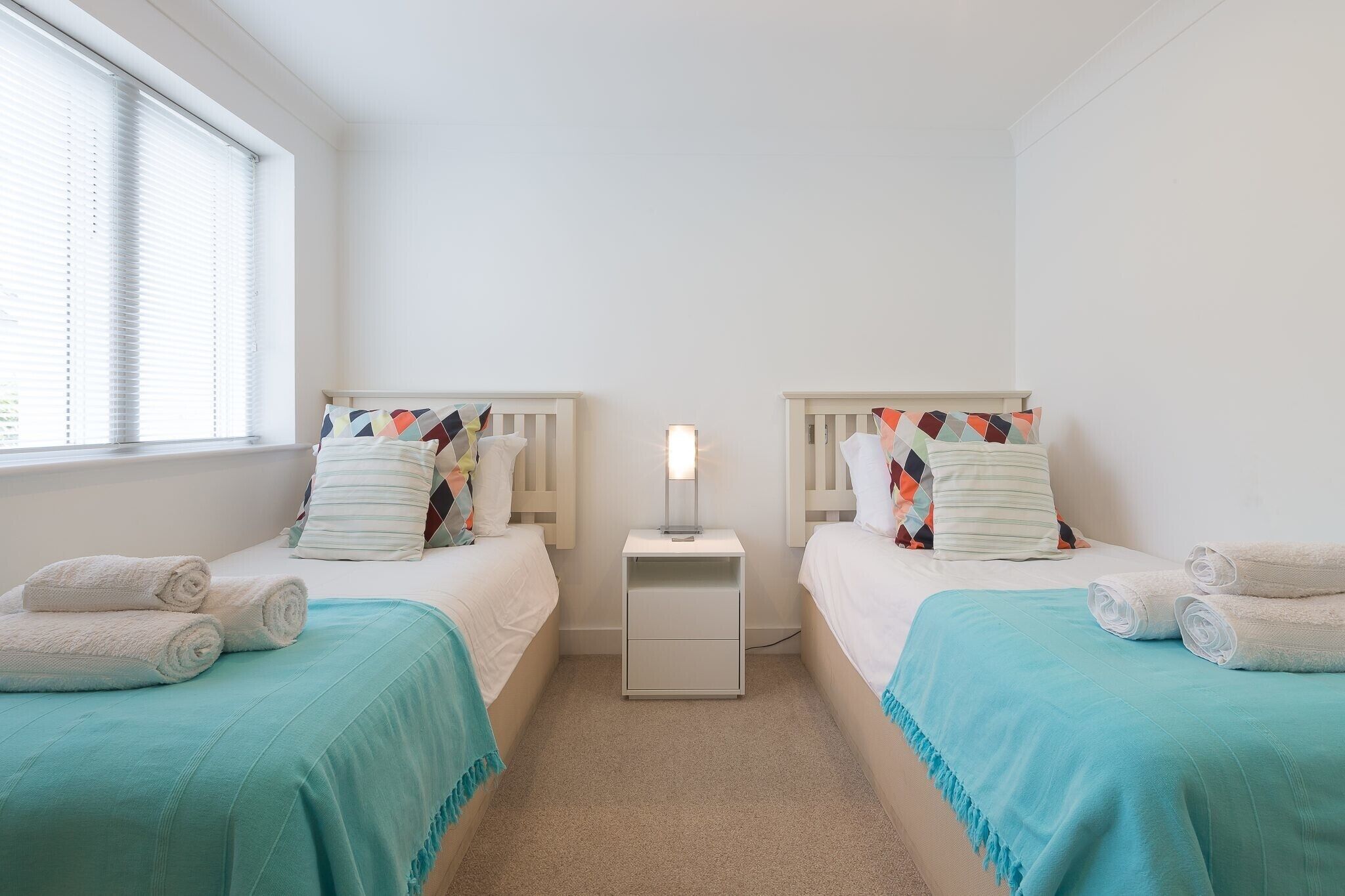 A twin bedroom with two beds, each with a colorful pillow and a white nightstand between them.