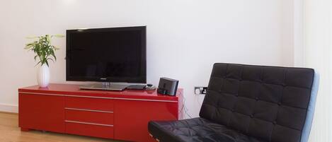 A modern living room with a red entertainment unit, a black leather sofa, a flat-screen TV, and a potted plant.