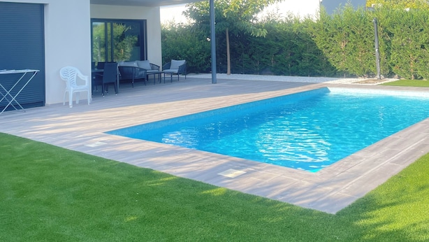 Una casa moderna con piscina, un patio con mobiliario exterior y un césped bien cuidado.