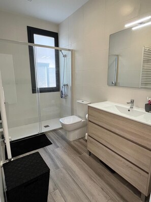 Moderni kylpyhuone, jossa on lasiseinällä varustettu suihku, wc ja peilillä varustettu pesuallas.