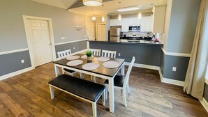 Un coin repas avec une table dressée pour quatre personnes, un banc et une cuisine en arrière-plan.