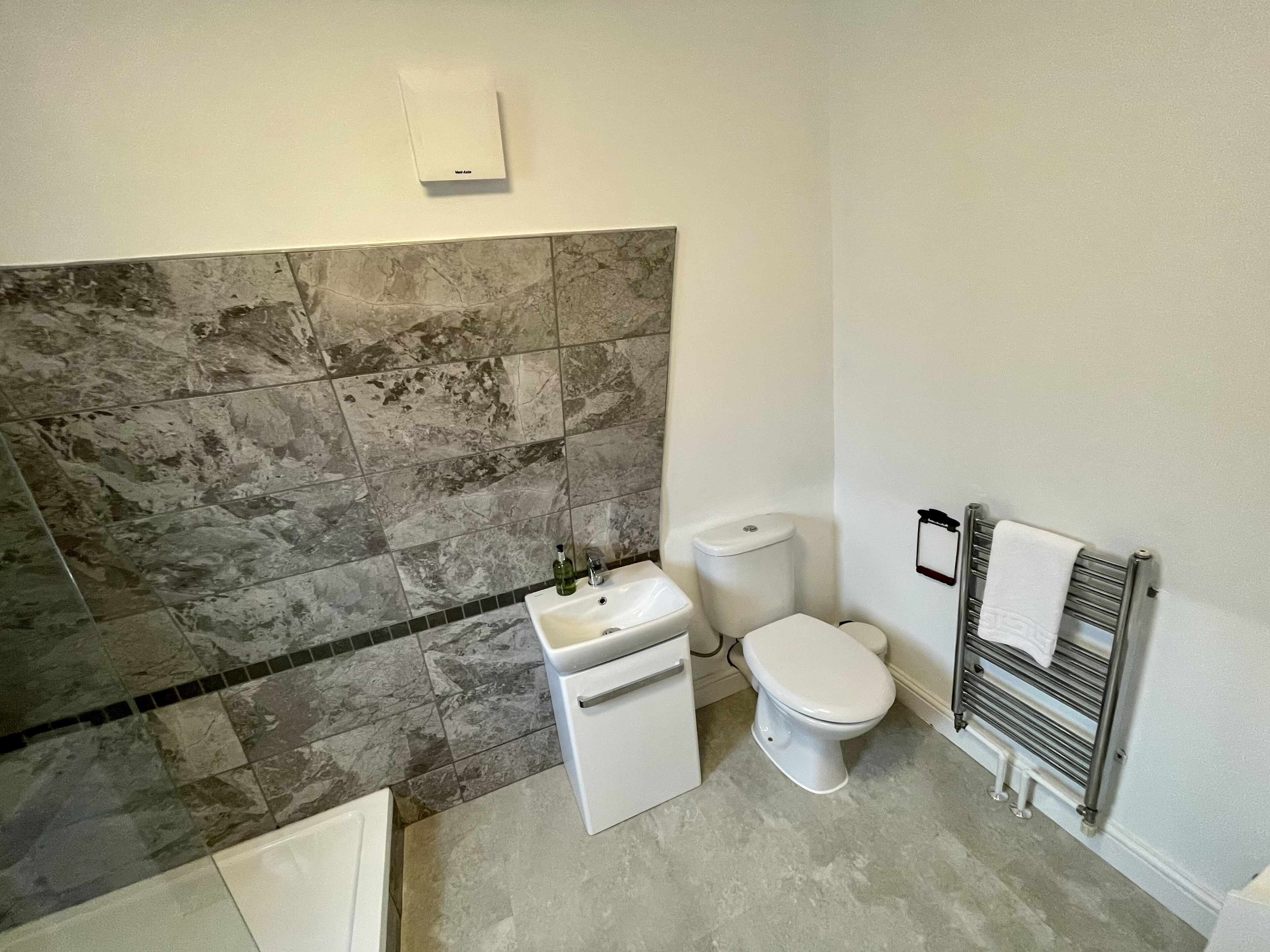 Un baño con pared de mármol, un lavamanos blanco, un inodoro y un perchero para toallas.