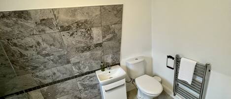 Un baño con pared de mármol, un lavamanos blanco, un inodoro y un perchero para toallas.