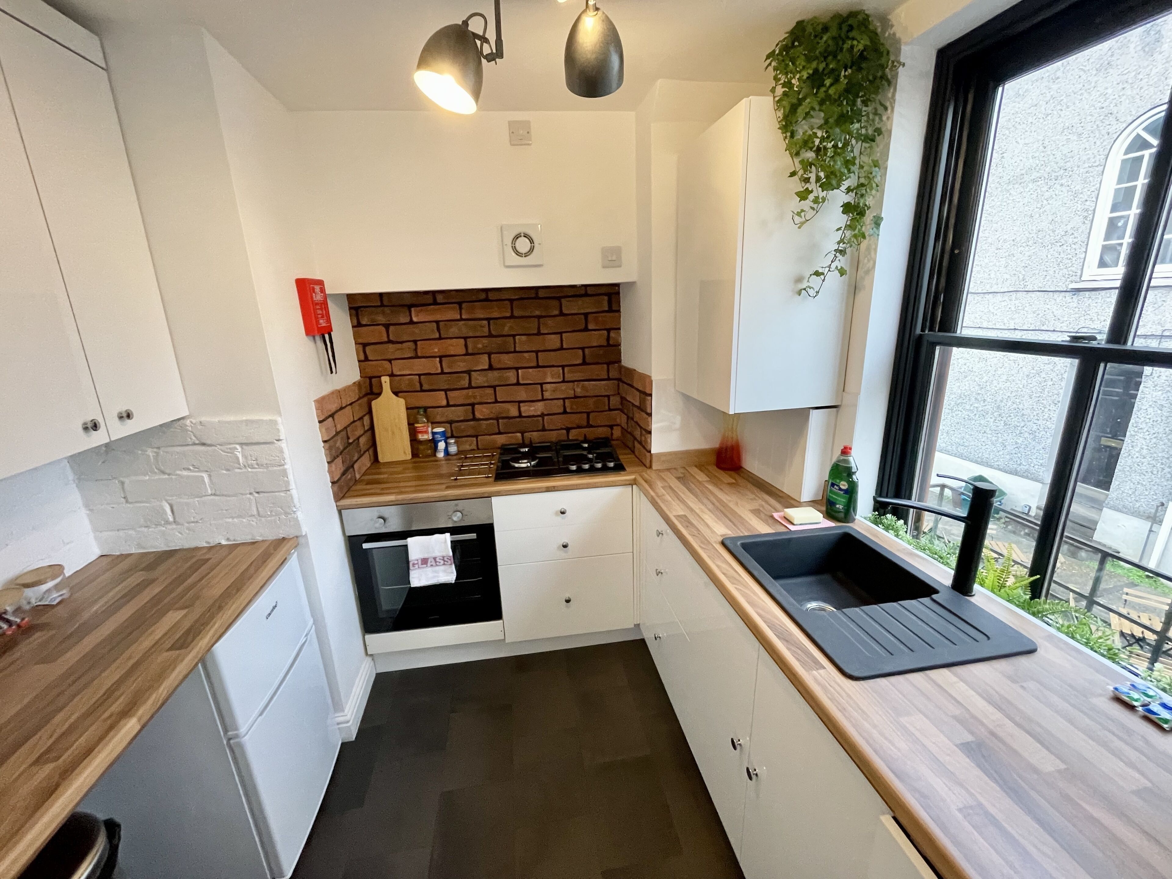 A modern kitchen with white cabinets, a brick backsplash, a gas stove, and a window with a view of the street.