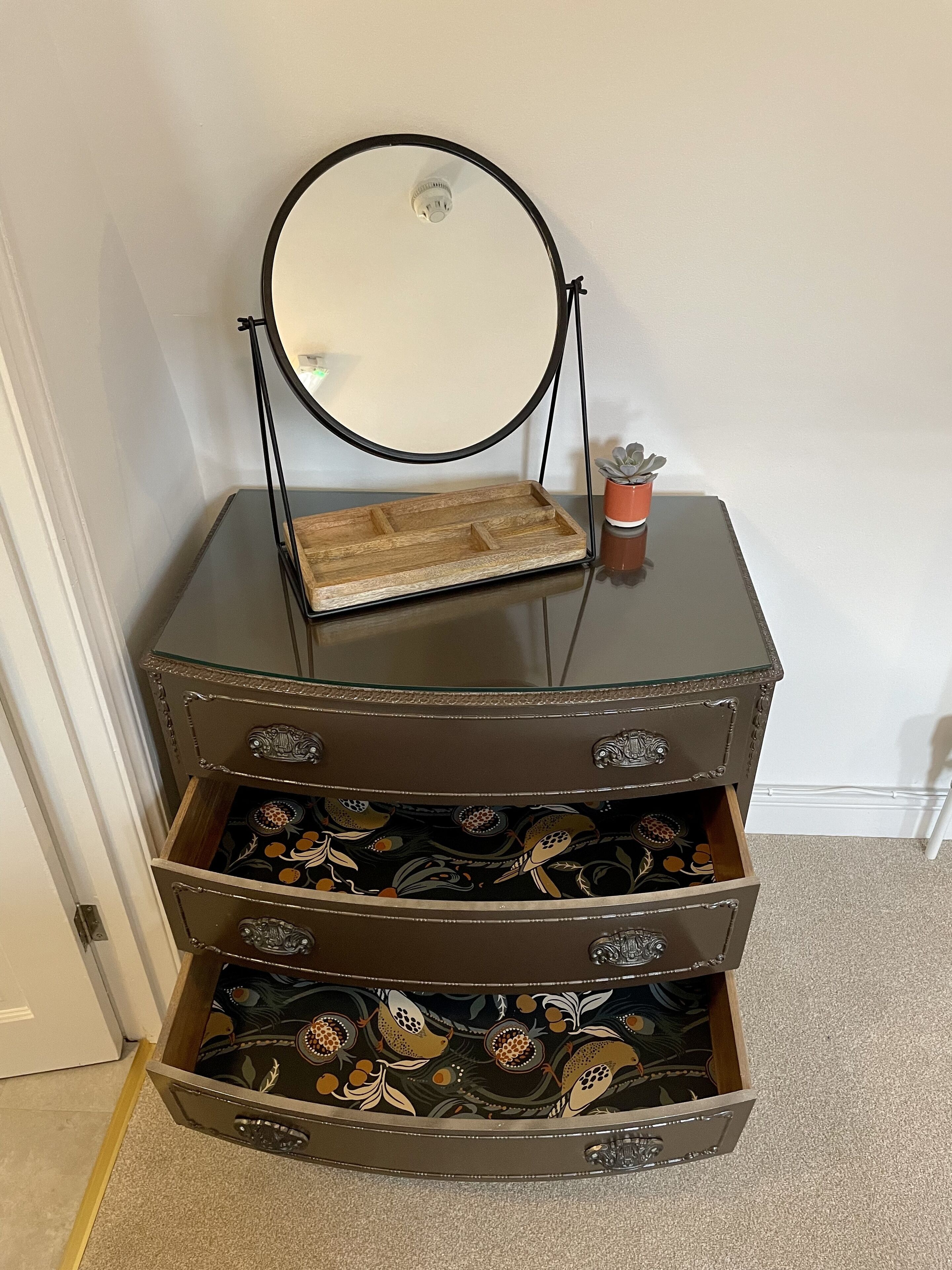 A dresser with a mirror, a tray, and a potted plant.