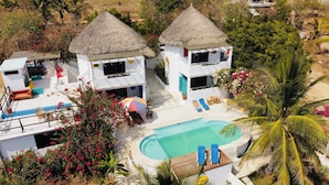 A resort with two thatched-roof buildings, a swimming pool, and tropical vegetation. - Beachfront villa is settled in Playa Agua Blanca 25 min from Puerto Escondido.  (Santa Maria Tonameca)