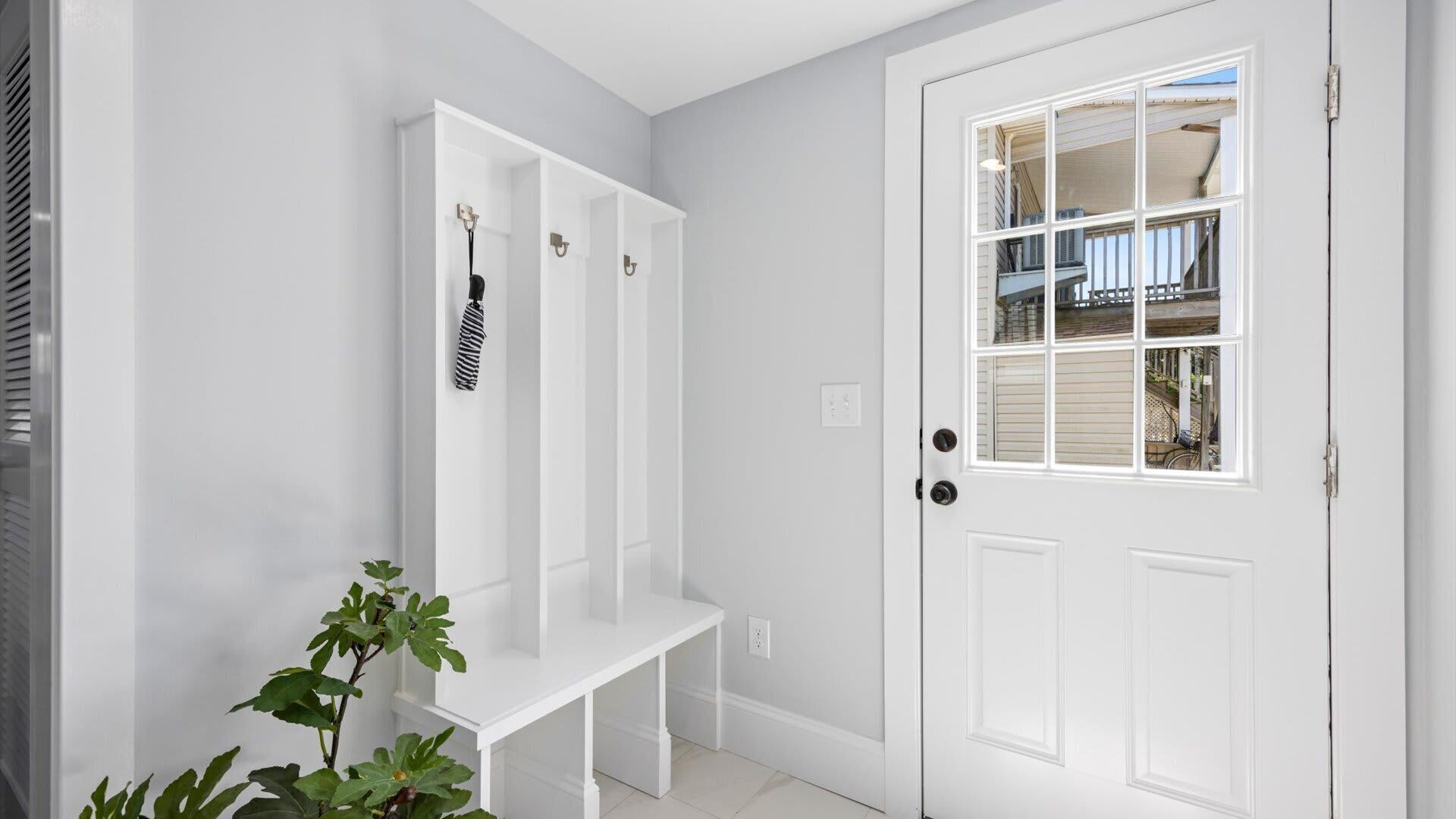 A white door with a window, a white bench, and a white wall with a vent.
